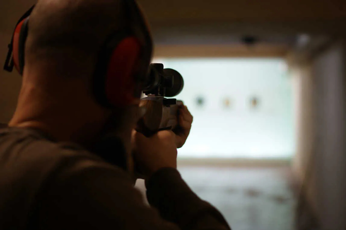 Shooter in the standing unsupported position with a scoped rifle at the sport rifle range.