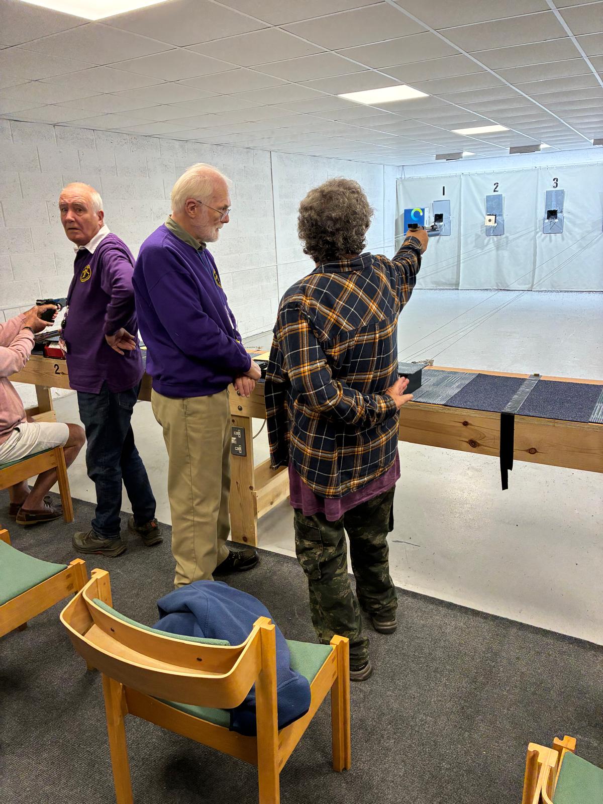 A guest shooting air pistol indoors with a Pinhoe member coaching beside them.